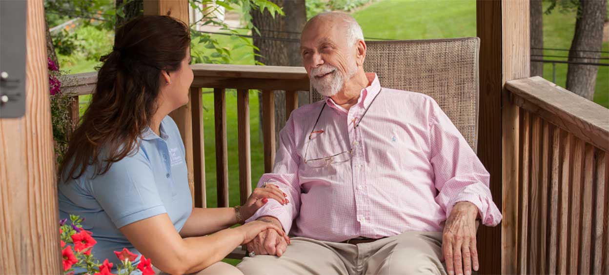 A caregiver comforts a patient sitting in a chair.