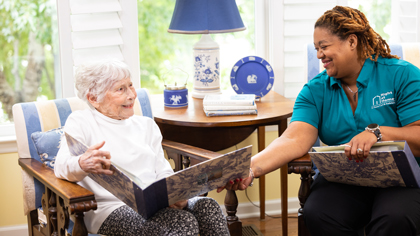 female caregiver and female senior client looking at photo albums while sitting down female caregiver and female senior client looking at photo albums while sitting down