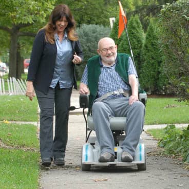 A female caregiver walks on the sidewalk with male senior in a wheelchair. A female caregiver walks on the sidewalk with male senior in a wheelchair.