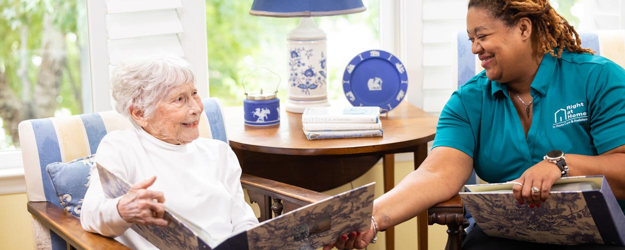 female caregiver and female senior client looking at photo albums while sitting down female caregiver and female senior client looking at photo albums while sitting down